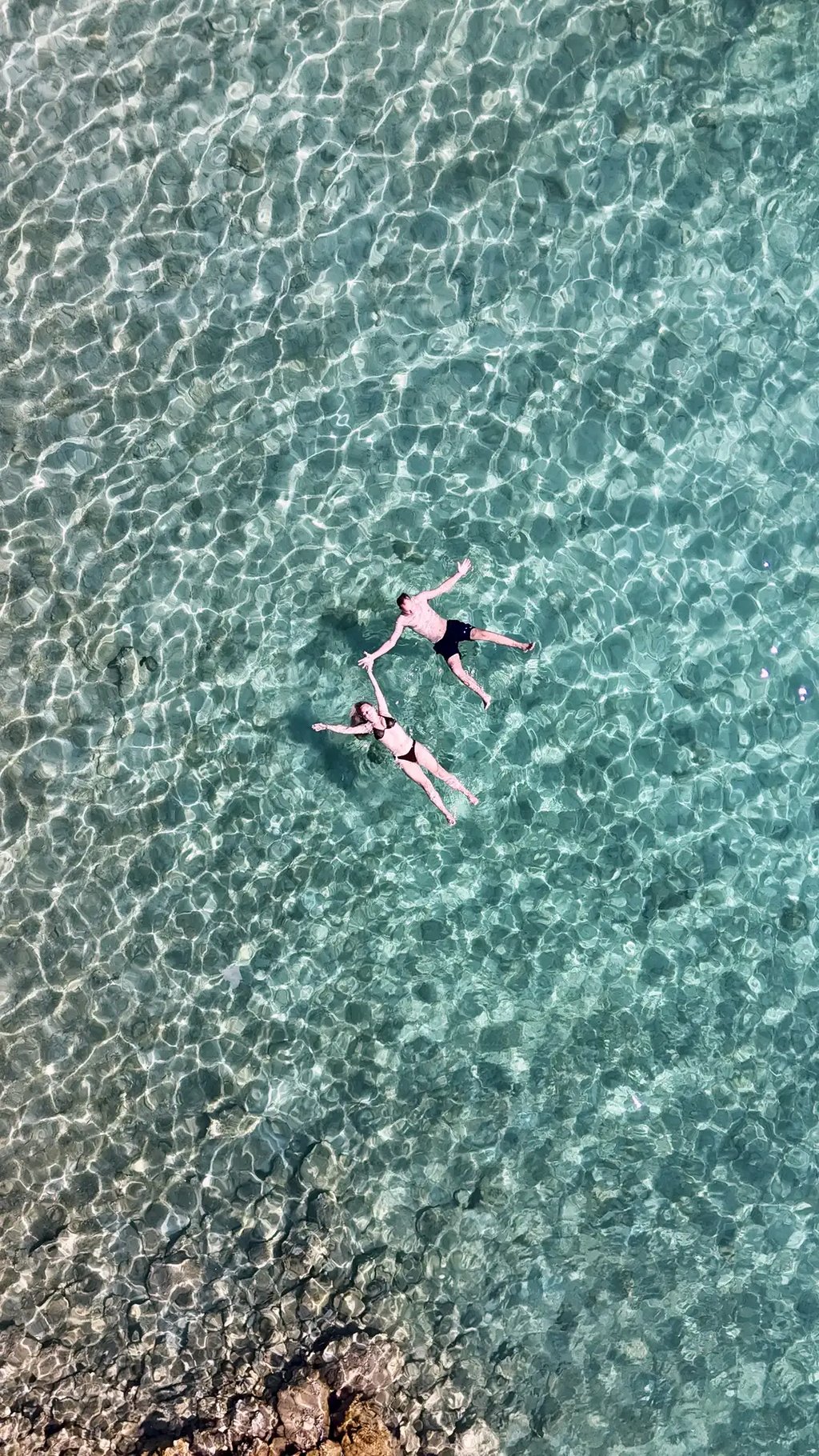 Couple floating in angel positions hand in hand in crystal clear Adriatic water captured by drone