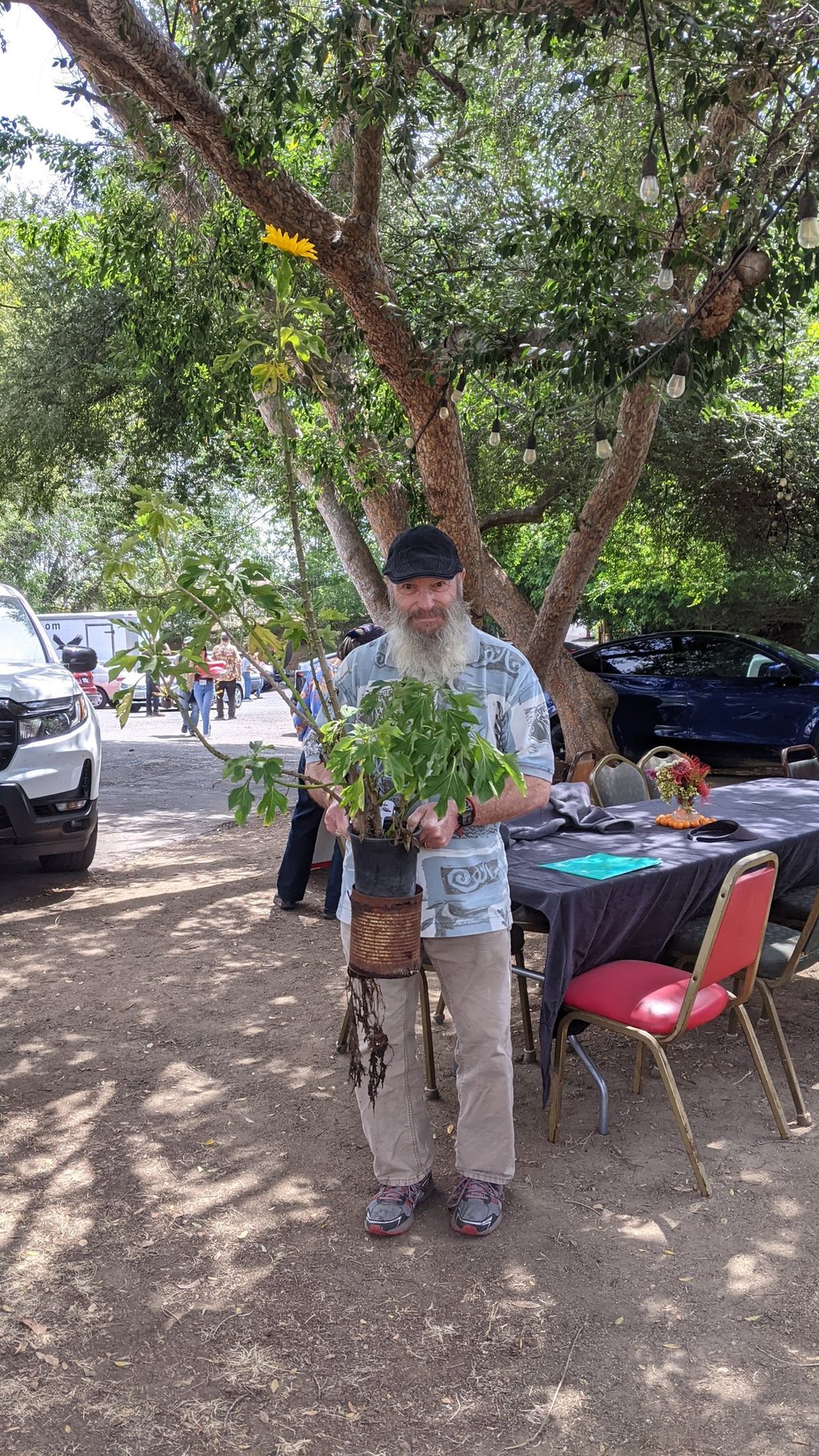 Man holding a tall plant in two stacked pots, with a slight smile
