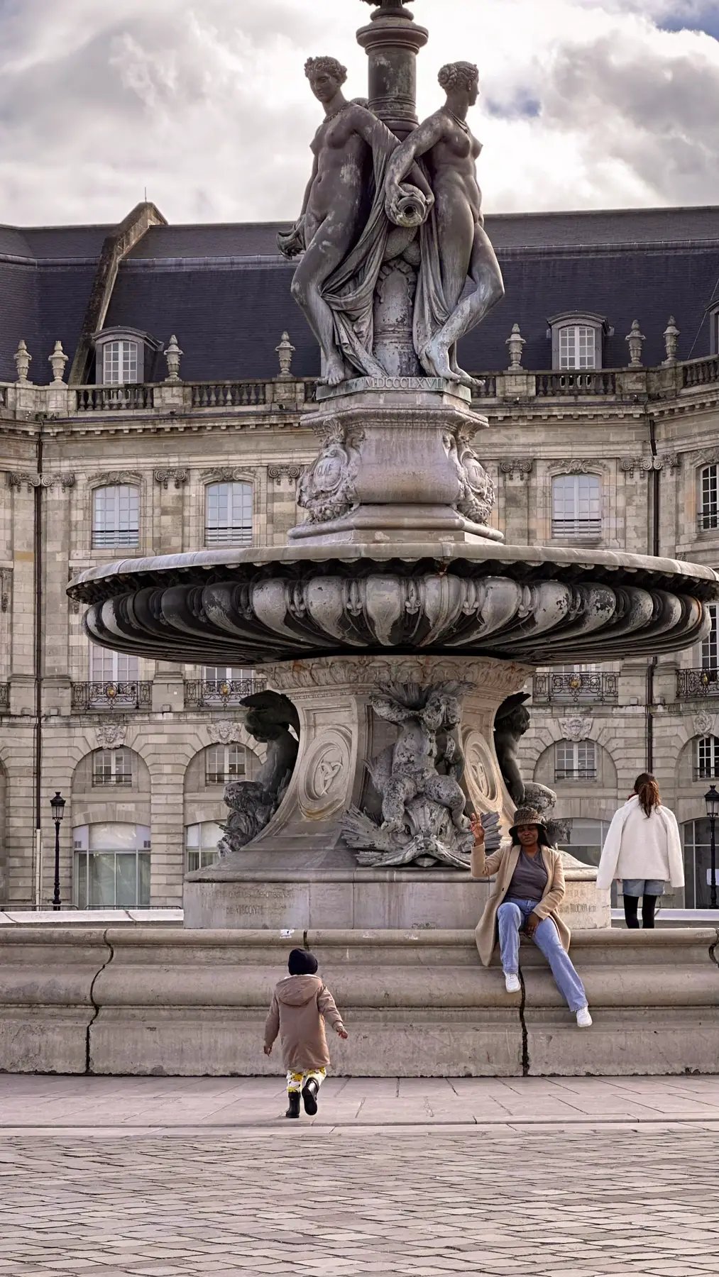 A woman sits on the Fountain of the Three Graces in Place de la Bourse, Bordeaux, France.