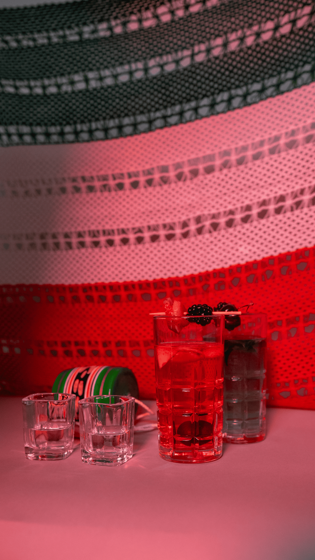 Red craft cocktails and tequila shots garnished with blackberries on a table with a Mexican flag background.