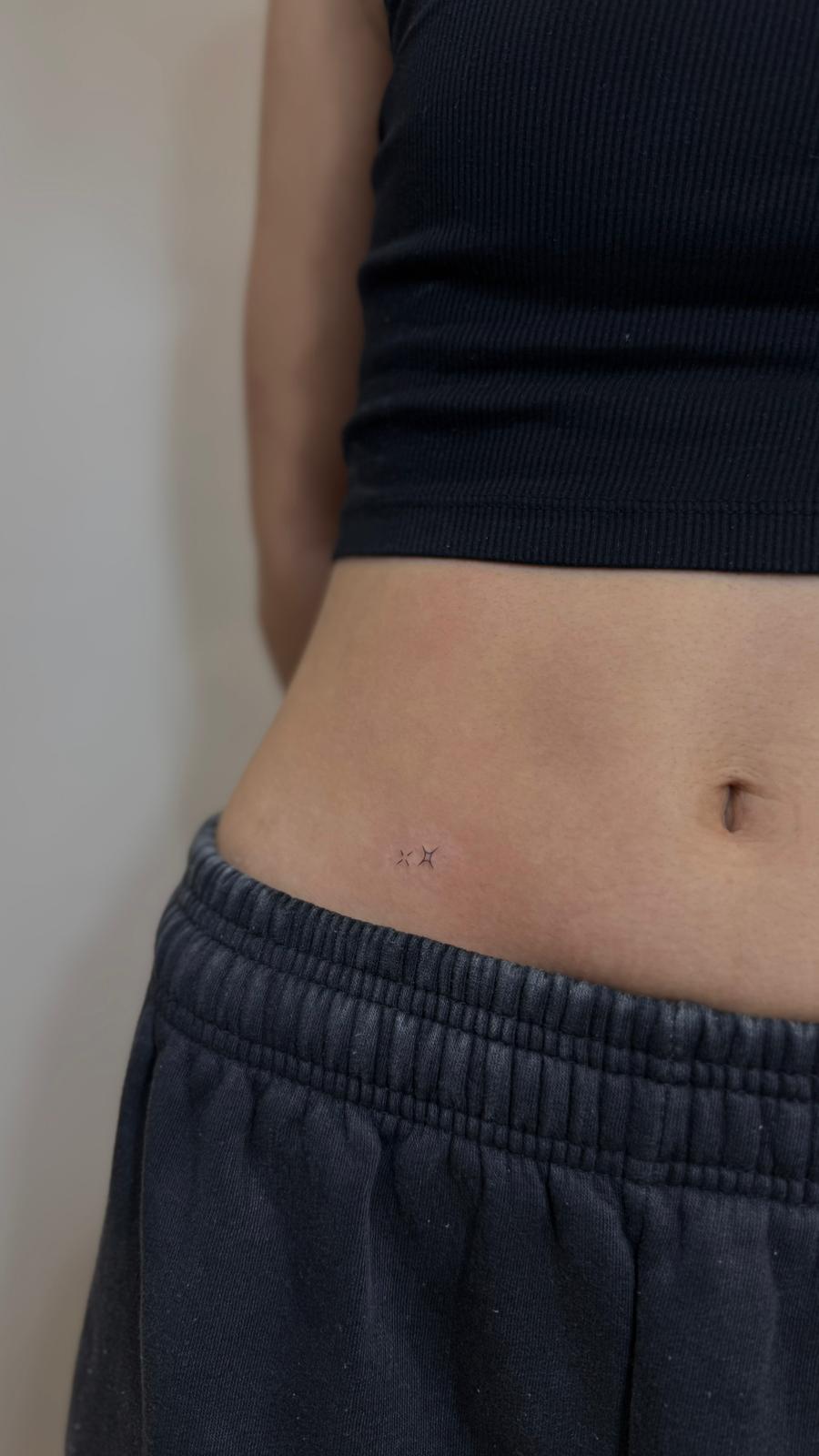 Tatuaje fineline en Madrid de dos estrellas de cuatro puntas micro en trazo fino en la cadera