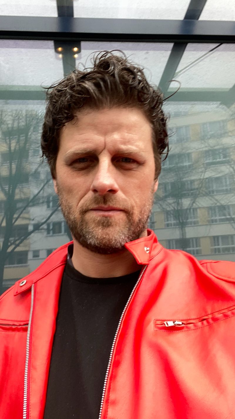 Rob Phillimore PR Consultant in Berlin, Germany wearing a red jacket and black t-shirt