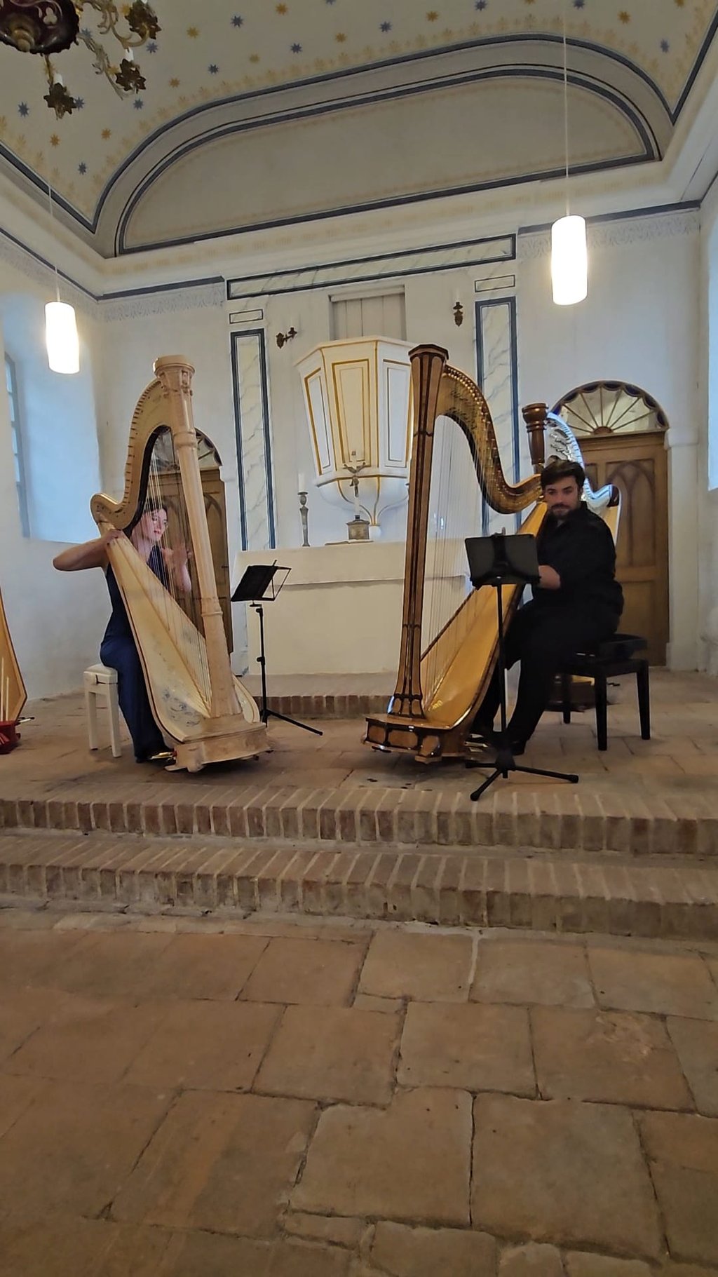 Maxi Treller und Clara Busemann sitzen jeweils an einer Harfe und spielen zusammen. Sie sind in einer Kirche