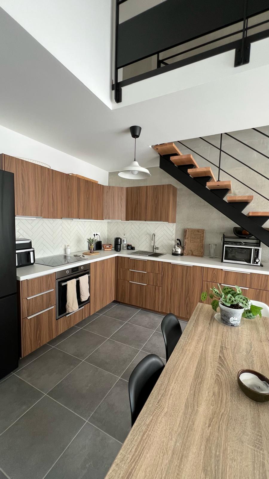 Modern kitchen with wood cabinets, herringbone tile backsplash, and a staircase in a loft apartment.