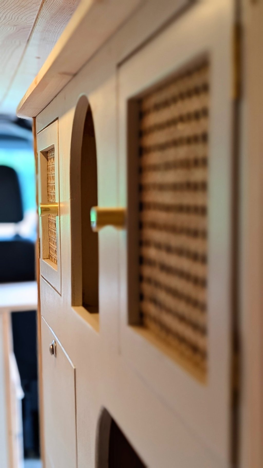 Zoom sur un meuble de van en bois avec porte en cannage naturel et poignées dorées, artisanat Pinbeu