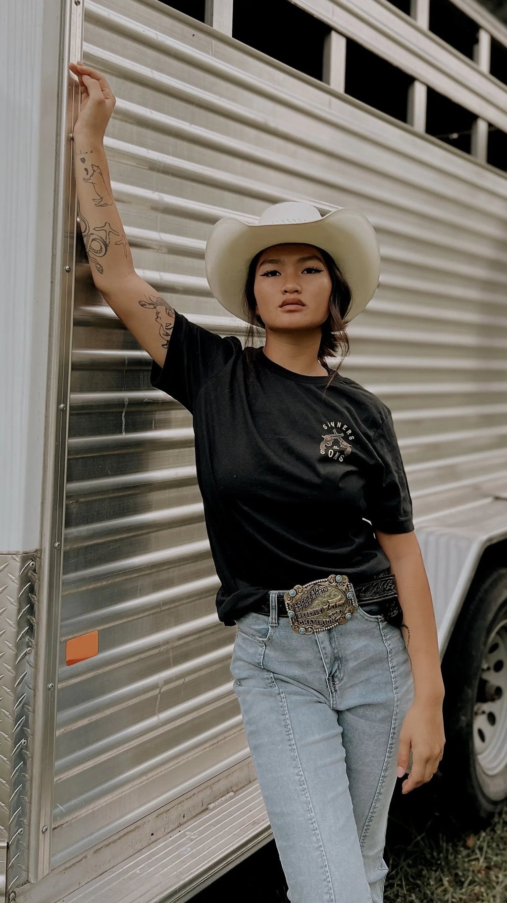 Woman in a black top and cowboy hat next to a horse trailer
