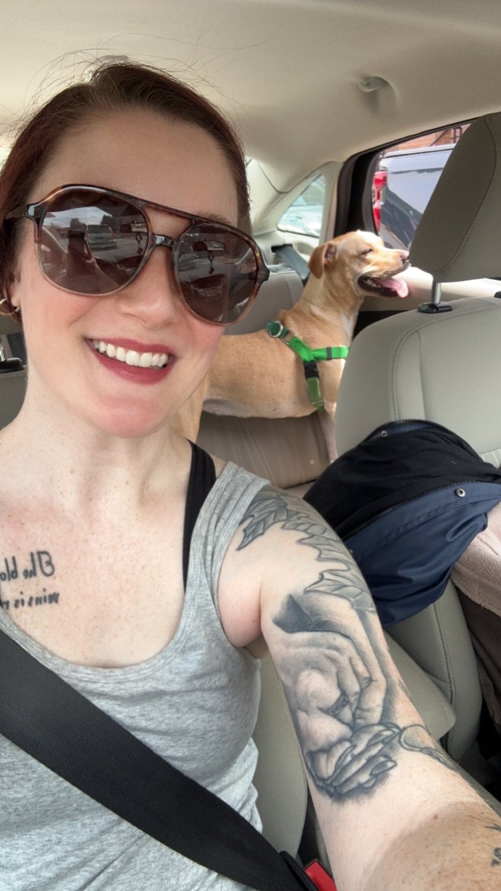 a woman with tattoos on her arm and a dog in the car