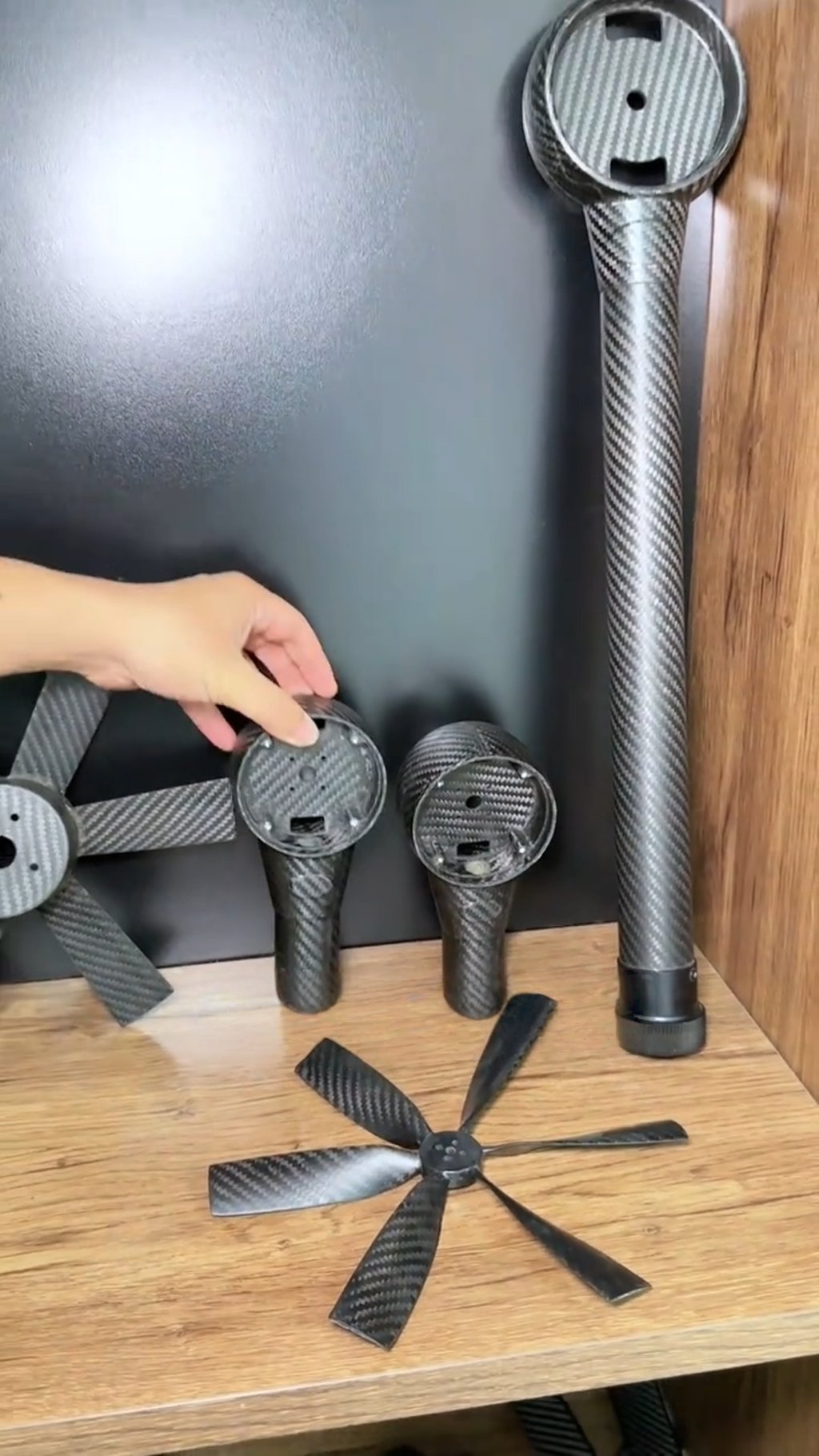 Custom lightweight carbon fiber drone parts including propeller blades and motor mounts on a wooden shelf.