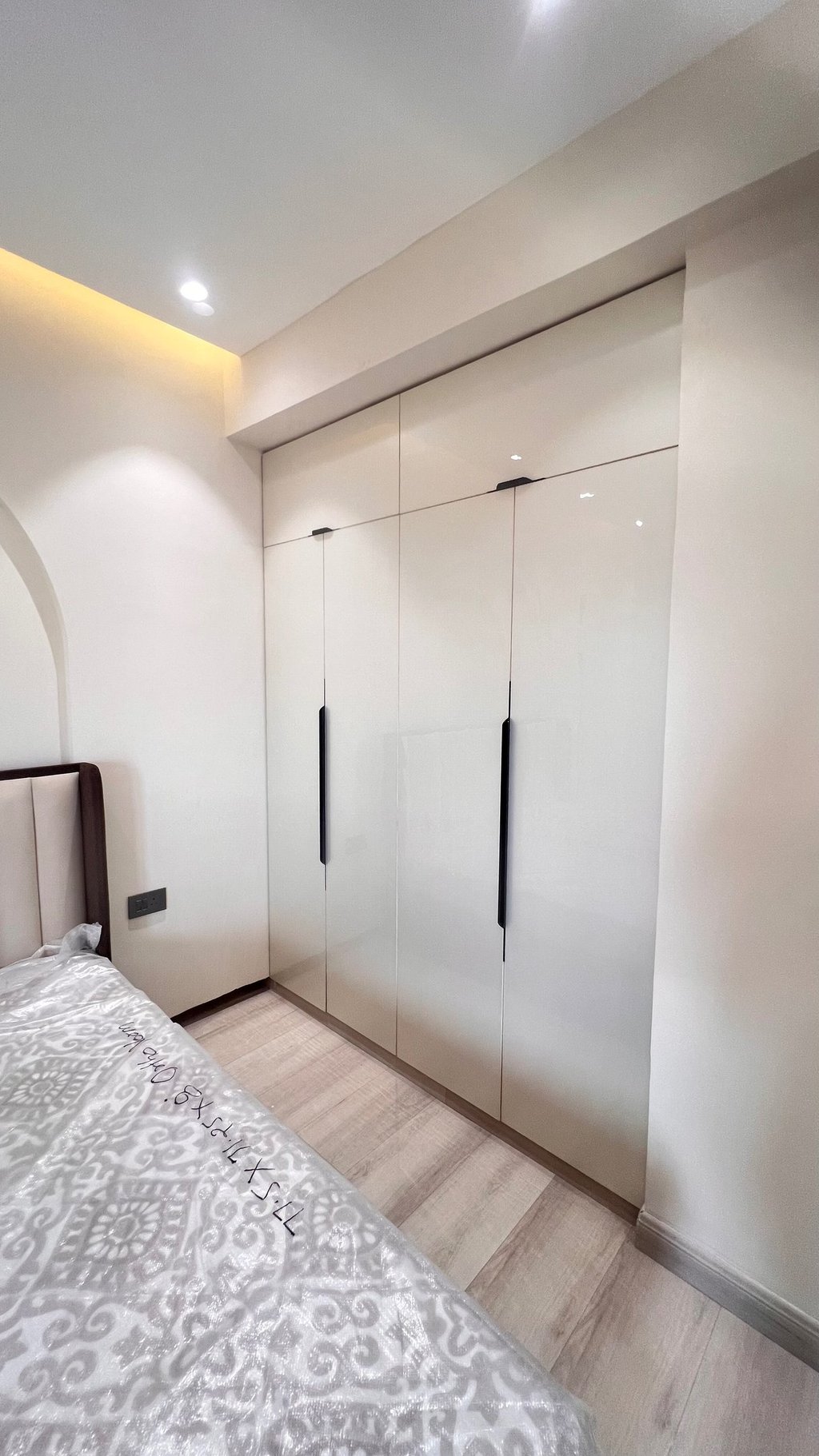 Modern white gloss fitted wardrobe with sleek black handles in a minimalist bedroom design.