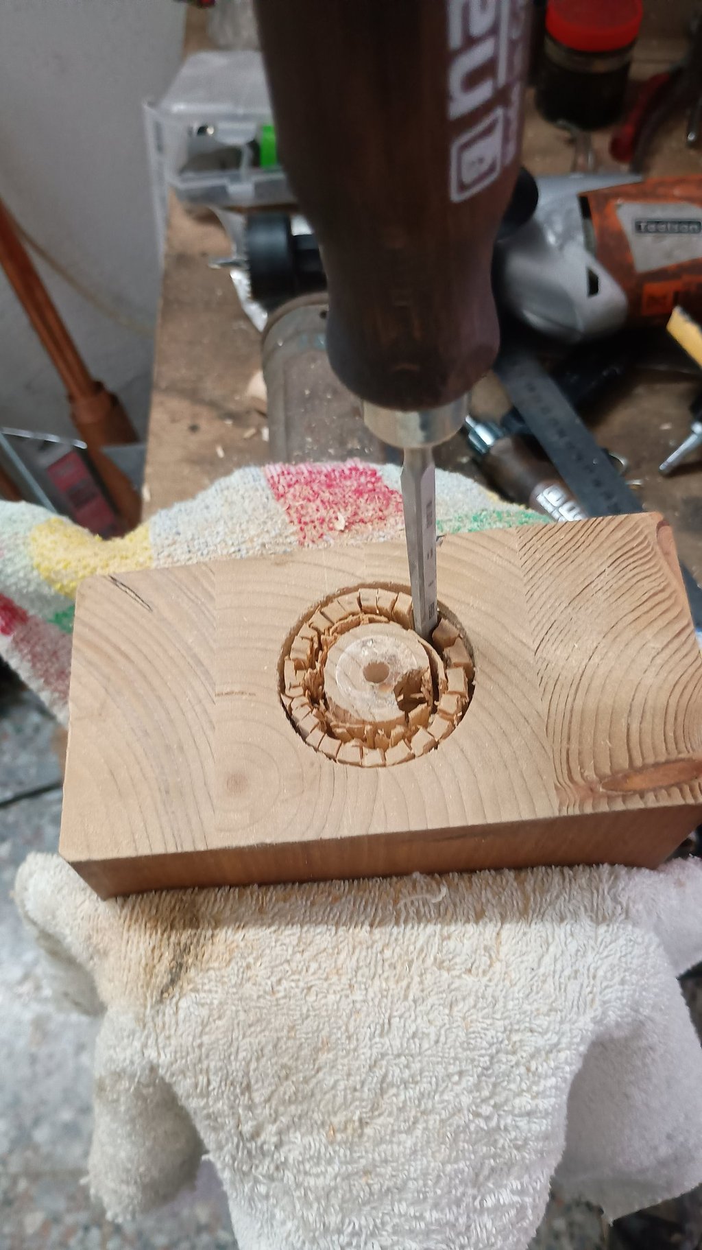 Hand chisel carving a circular recessed hole into a wooden block on a workbench.