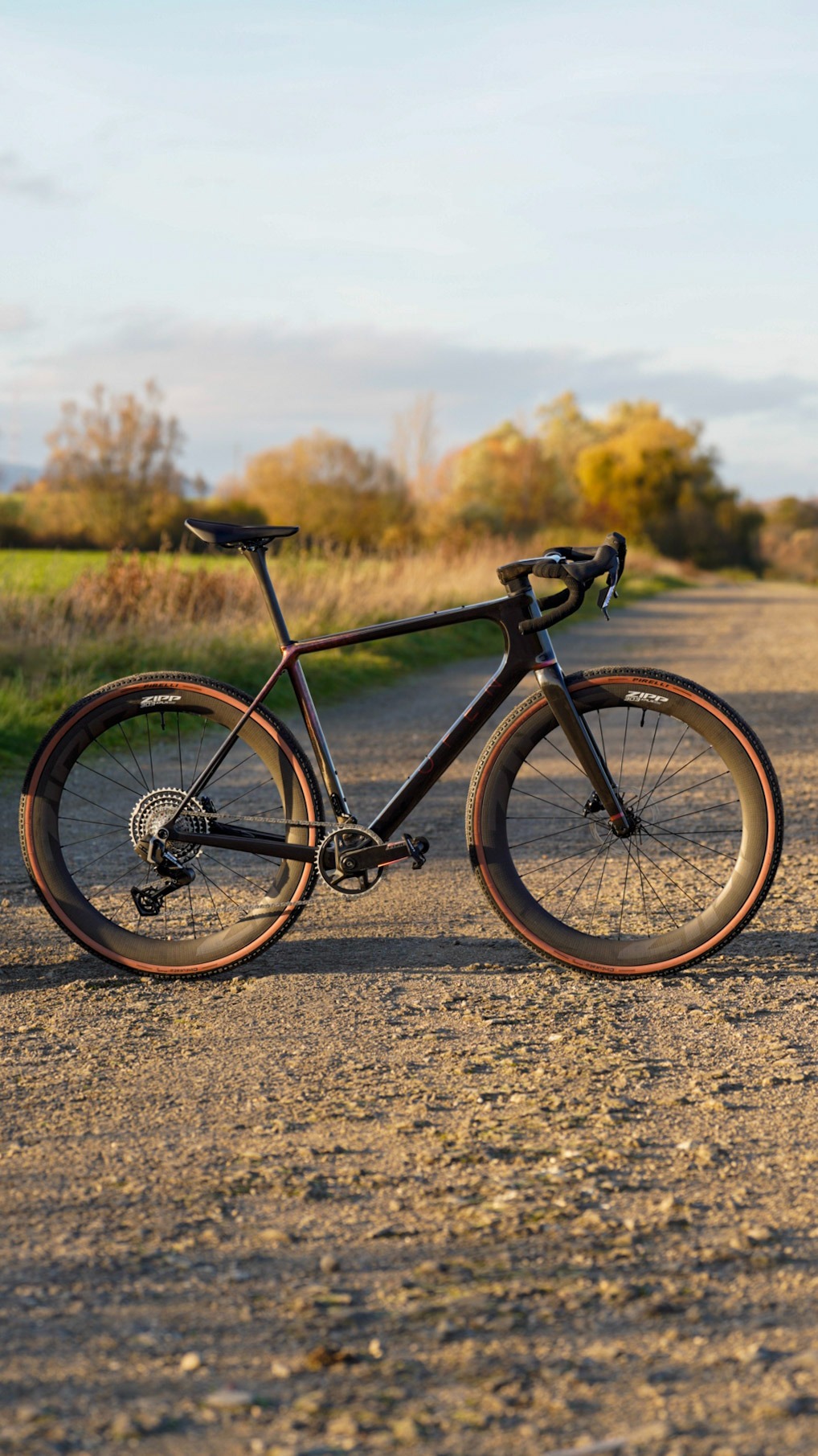 A high-performance carbon gravel bike with Zipp wheels on a sunny dirt trail.