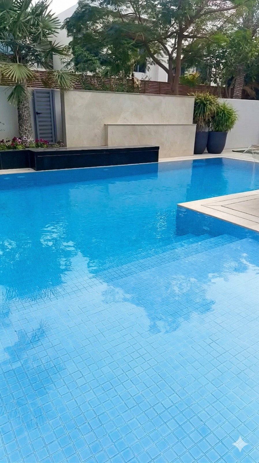 Luxury backyard swimming pool with blue tiles, stone water feature, and tropical landscaping.