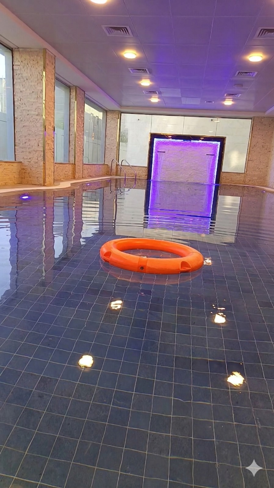 Luxury indoor swimming pool with blue tiles, an orange lifebuoy, and purple LED lighting accents.