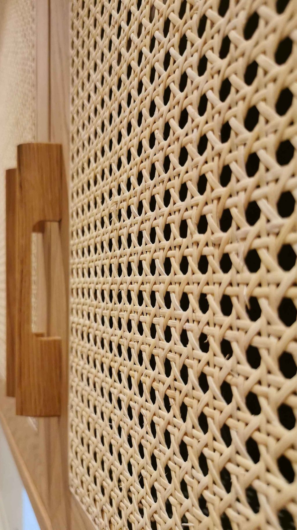 Close-up of a natural rattan webbing cabinet door with a wooden handle for boho home decor.