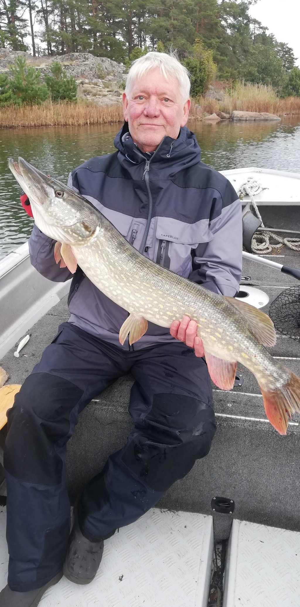 un homme est assis dans un bateau de pêche en suède, il a un beau brochet.