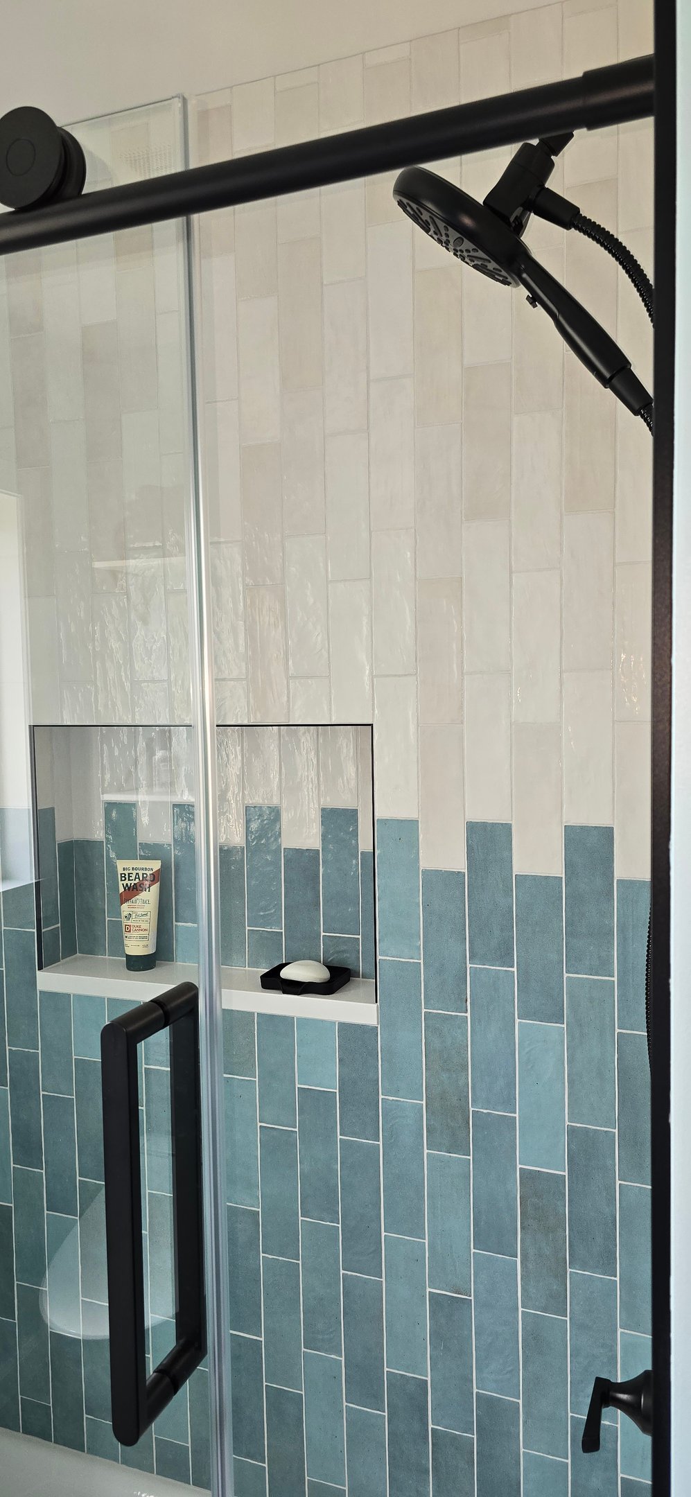 Modern walk-in shower with vertical blue and white subway tiles, glass doors, and black hardware.