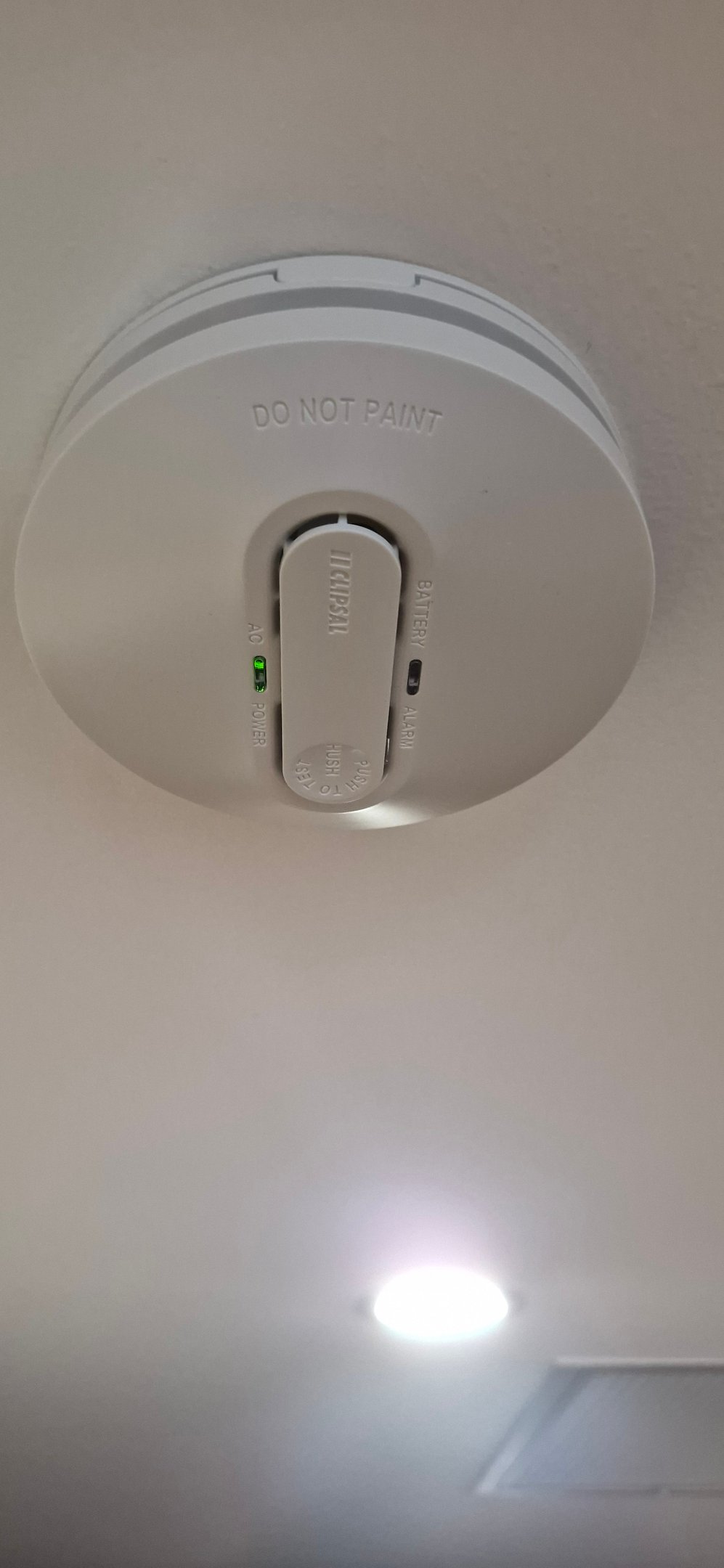 White Clipsal smoke alarm installed on a ceiling with green AC power indicator light.