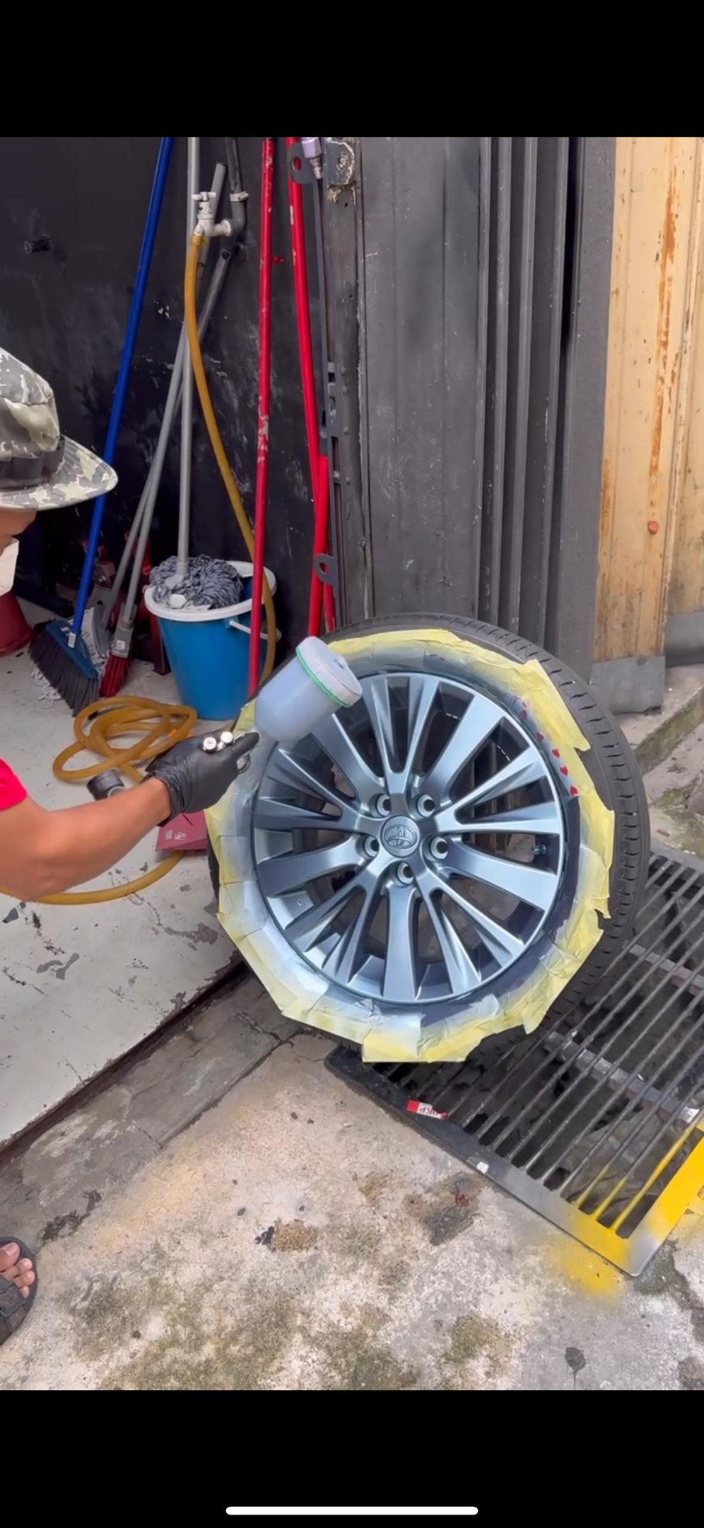 Technician spray wrapping car wheel rim in matte silver finish