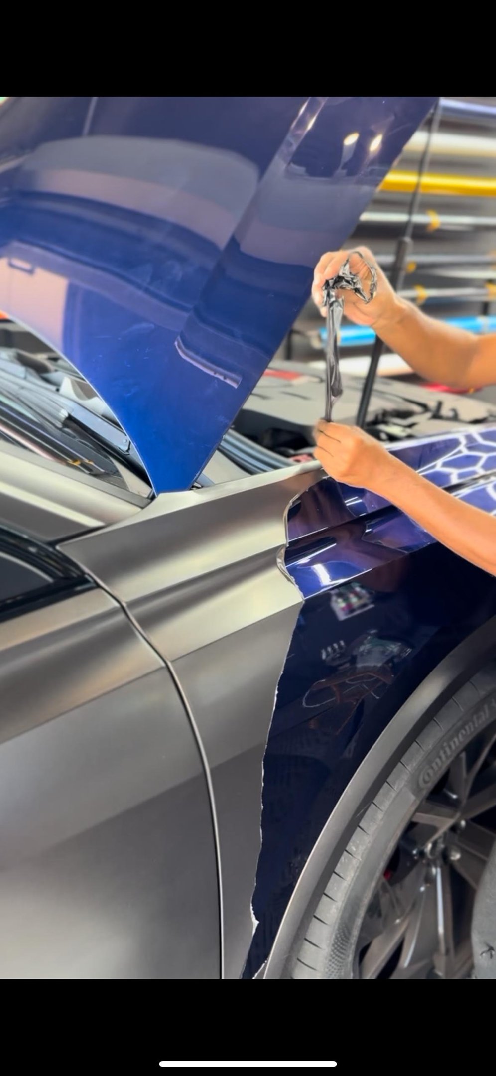 Technician peeling protective film from navy blue vinyl wrap