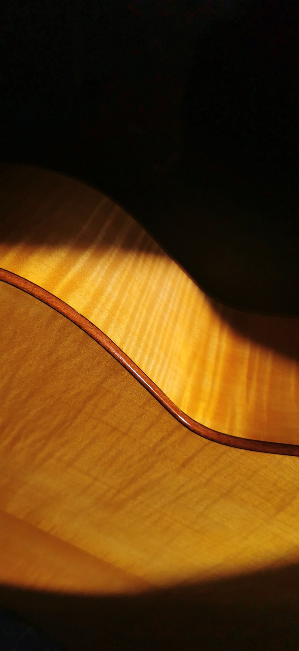 Close-up of a acoustic guitar with a natural flamed maple wood, and french finish and dark binding.