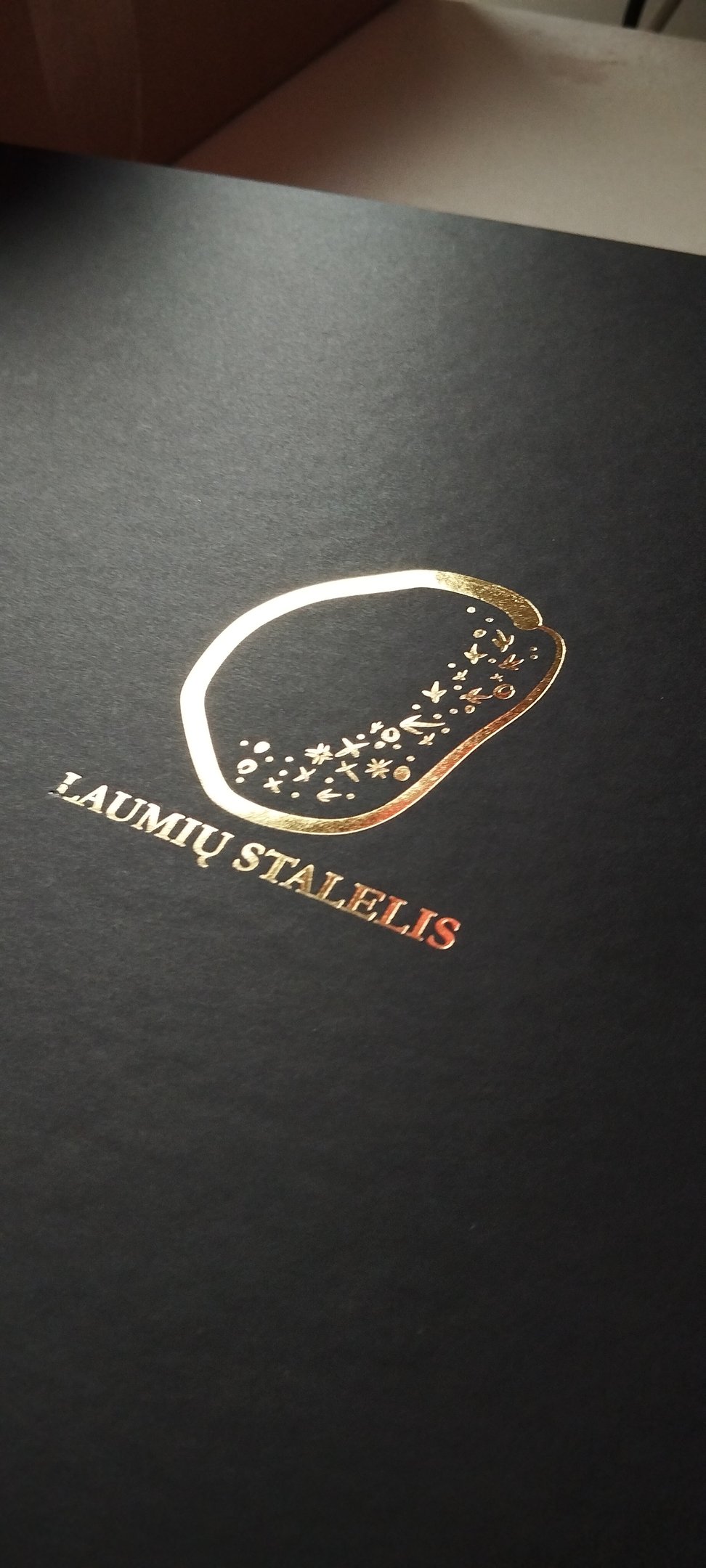 Luxury black matte gift box featuring a gold foil Laumių Stalelis logo with celestial star patterns.