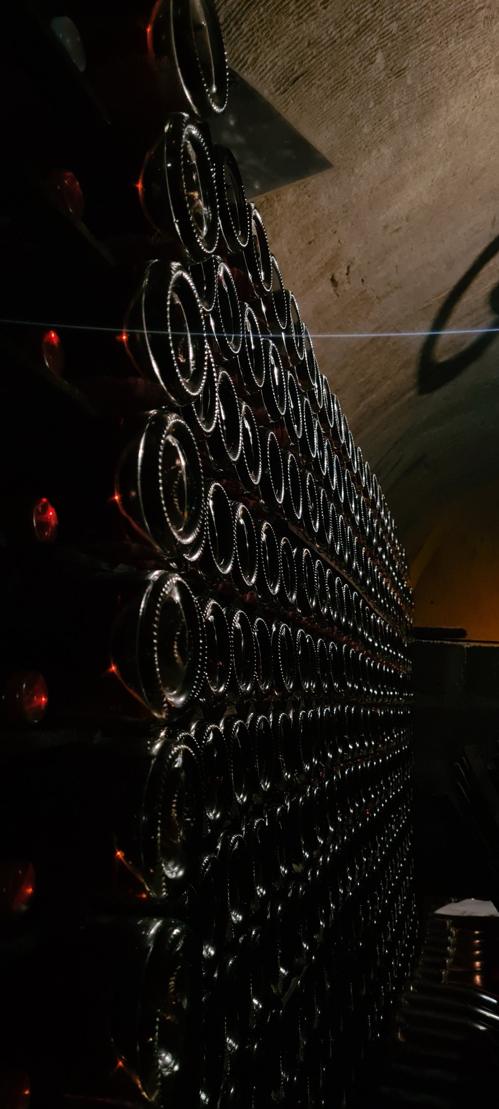 Atmospheric view of champagne bottles aging in a historic underground cellar, captured in dramatic low light.