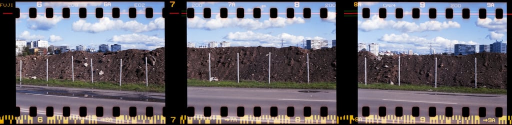 Composed photo featuring a street with a prominent, dark, rocky mound, with the cityscape in the background and clouds on sky