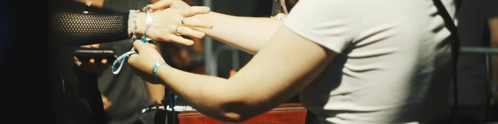 A staff member secures a festival wristband on a guest's arm at a concert event entrance.