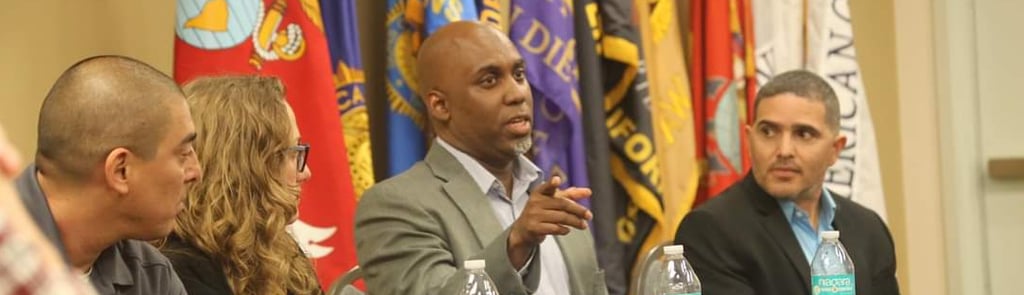 Lee A Jones in a suit and tie is sitting at a table  with a microphone