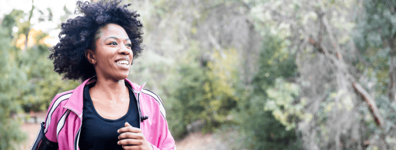Une jeune femme noire souriante aux cheveux naturels et une veste de sport rose qui fait son jogging