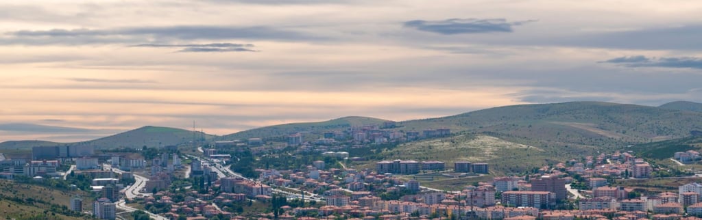 Panoramic aerial view of a Turkish city nestled in rolling hills under a cloudy sunset sky.