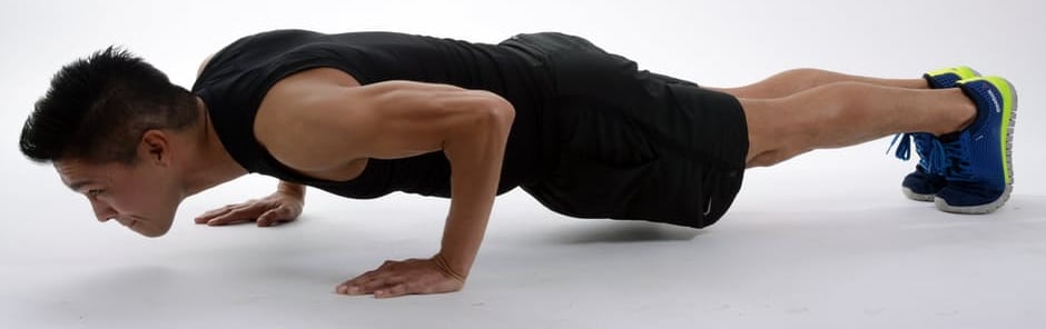A person with lean arm muscles is in plank position in a white room.