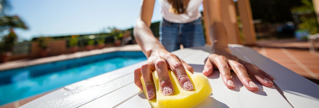 donna che fa le pulizie al sole con una spugnetta gialla con il sapone che pulisce un tavolo bianco