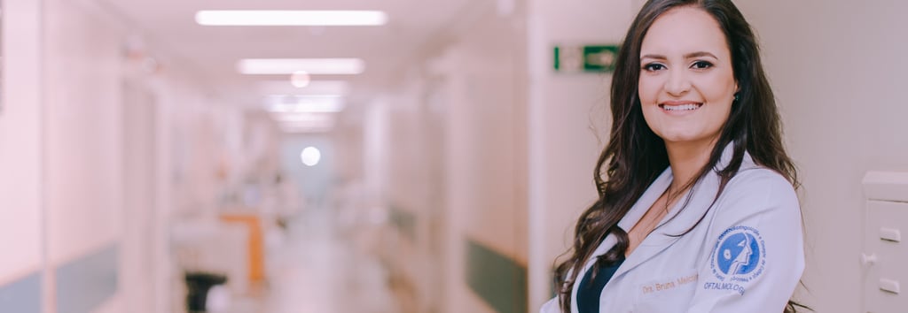 Dra Bruna Melchior de jaleco branco sorrindo de braços cruzados, aos fundos um corredor do hospital das clinicas da USP