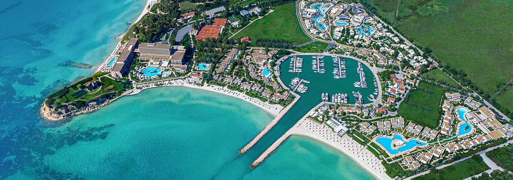 Aerial view of  Sani Resort Halkidiki, Greece with a private yacht marina and turquoise ocean water.