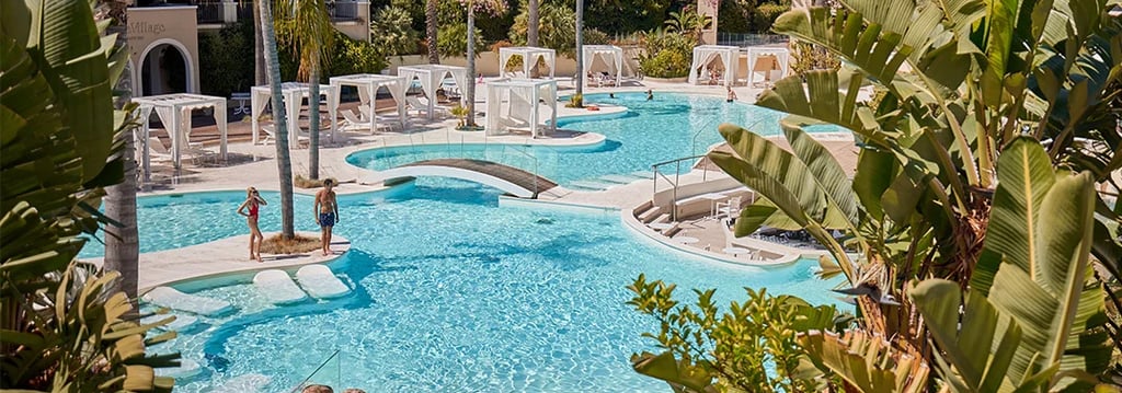 Luxury tropical resort swimming pool with white cabanas, palm trees, and turquoise water.