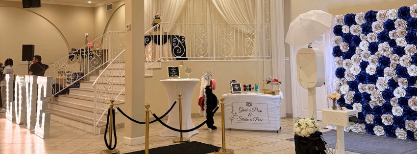 Wedding photo booth rental with blue and white paper flower backdrop, props table, and white kiosk.