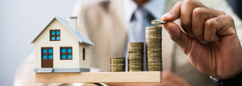 a man in a suit and tie is holding a house on a scale with coins