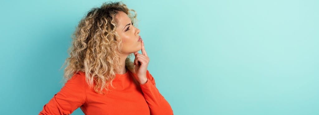 A curly-haired woman putting a finger to her chin, deep in thought
