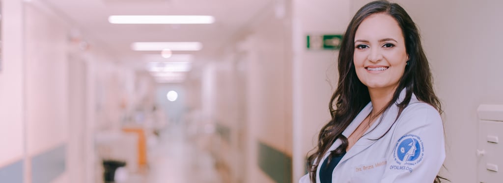 Dra Bruna Melchior de jaleco branco sorrindo de braços cruzados, aos fundos um corredor do hospital das clinicas da USP