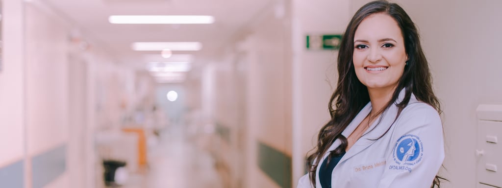 Dra Bruna Melchior de jaleco branco sorrindo de braços cruzados, aos fundos um corredor do hospital das clinicas da USP