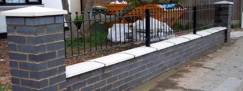 Blue perfurated engineering brick wall with white coping, caps and black railngs