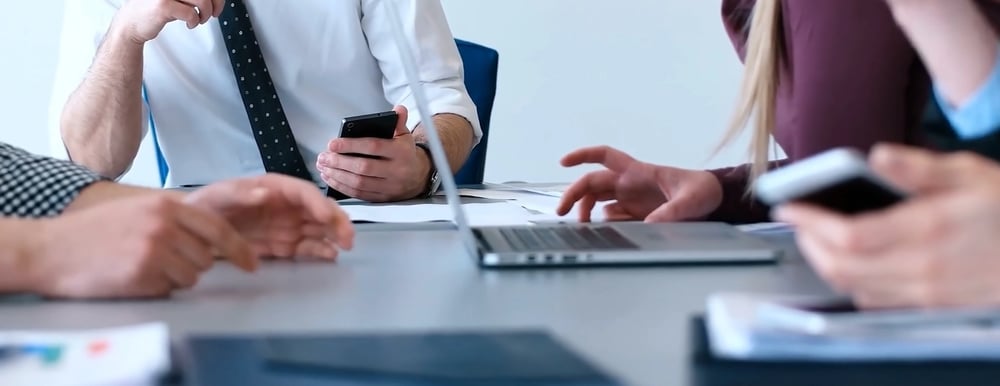 A distracted office leader checking phone notifications during a professional meeting