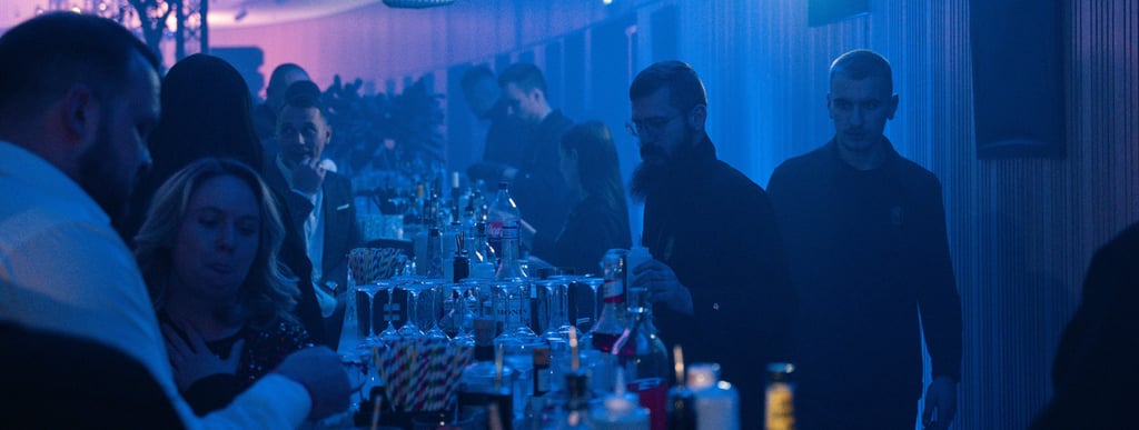 Stilingas baras vakarėlio metu, apšviestas mėlyna šviesa, su profesionaliais barmenais ir svečiais