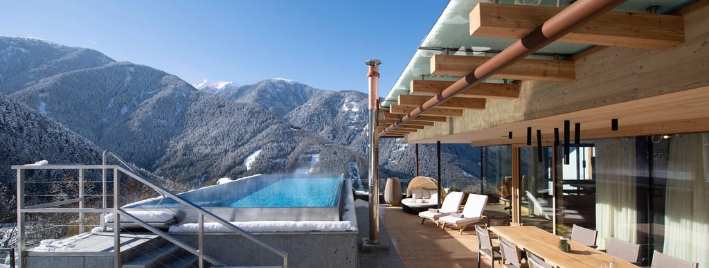 Luxury rooftop terrace with infinity pool overlooking snow-covered mountains in a winter resort.