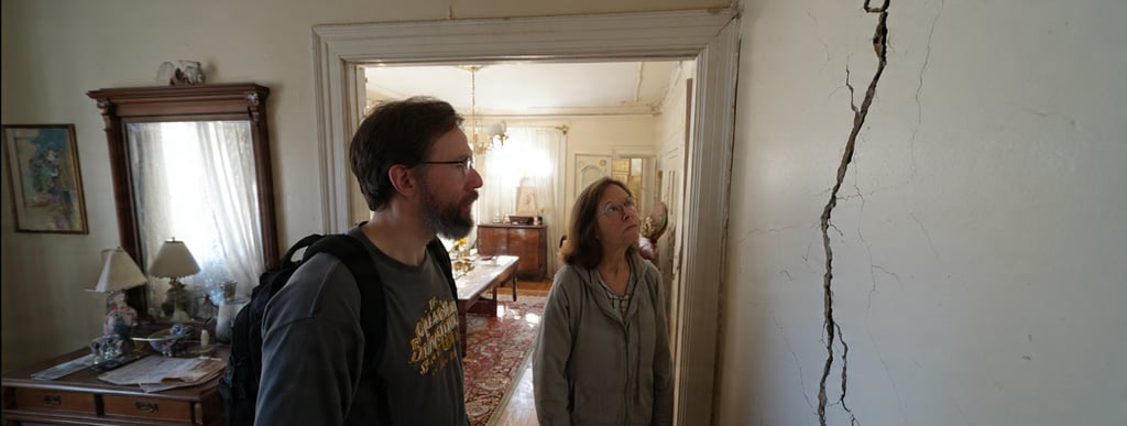Two people inspecting a large wall crack above a doorway inside an older home in Virginia