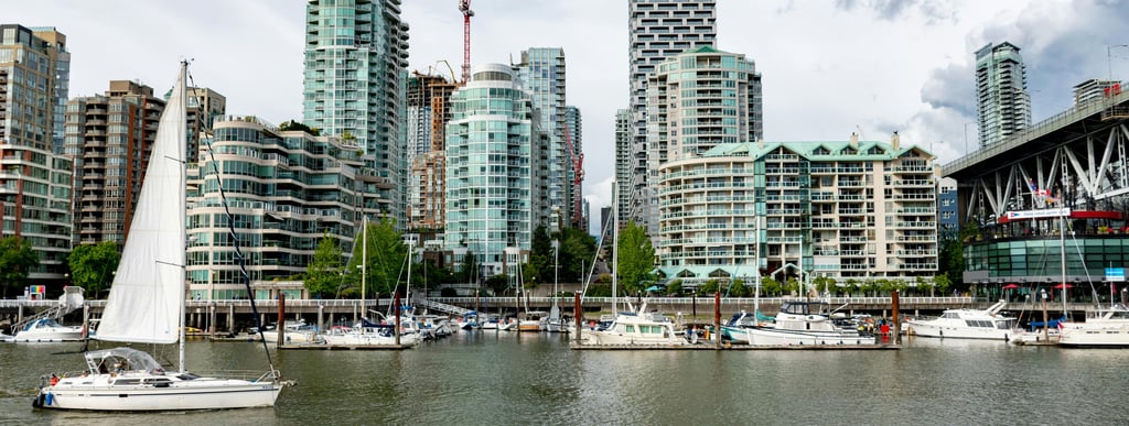 A waterfront scene with high-rise buildings, including some under construction, and sailboats docked along the shore.