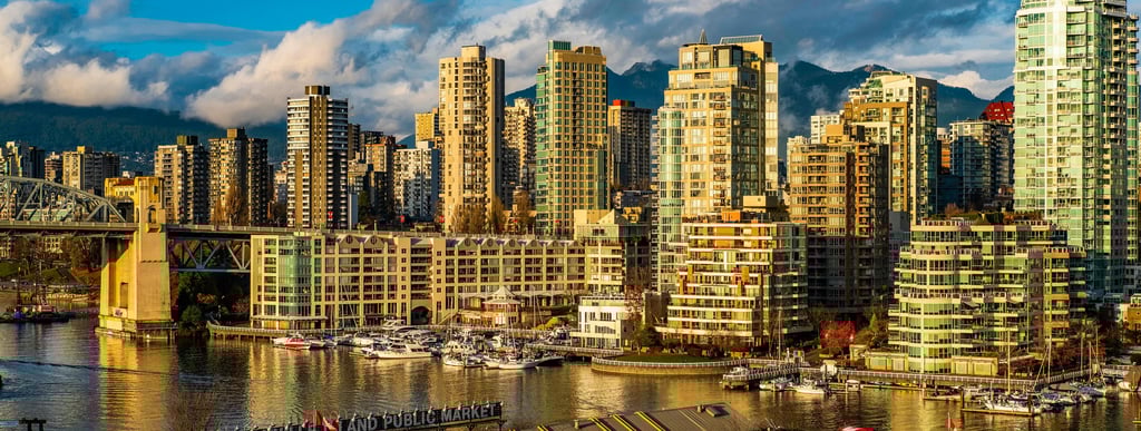 A wide panoramic view of the same waterfront city, with bridges, yachts, and a vibrant skyline under partly cloudy skies.