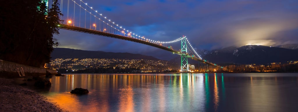 Lions Gate Bridge at night with lights reflecting on the water.