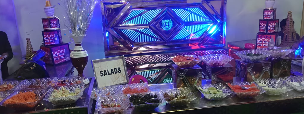 Buffet setup with assorted salads in glass bowls, a 'SALADS' sign, blue and purple lighting.